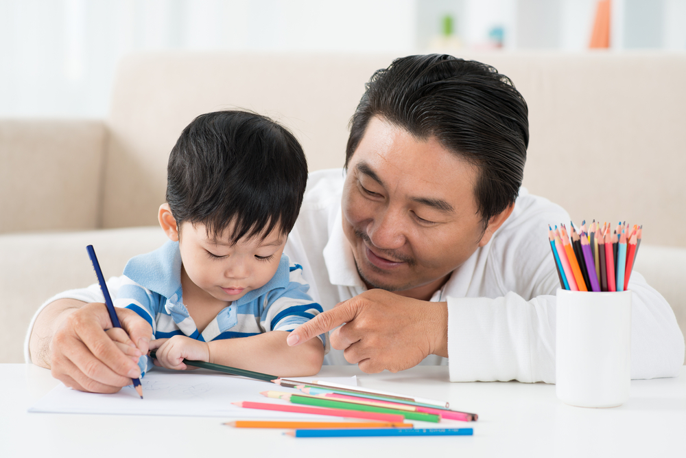 Father teaches son coloring, that helps with fine motor skills too.